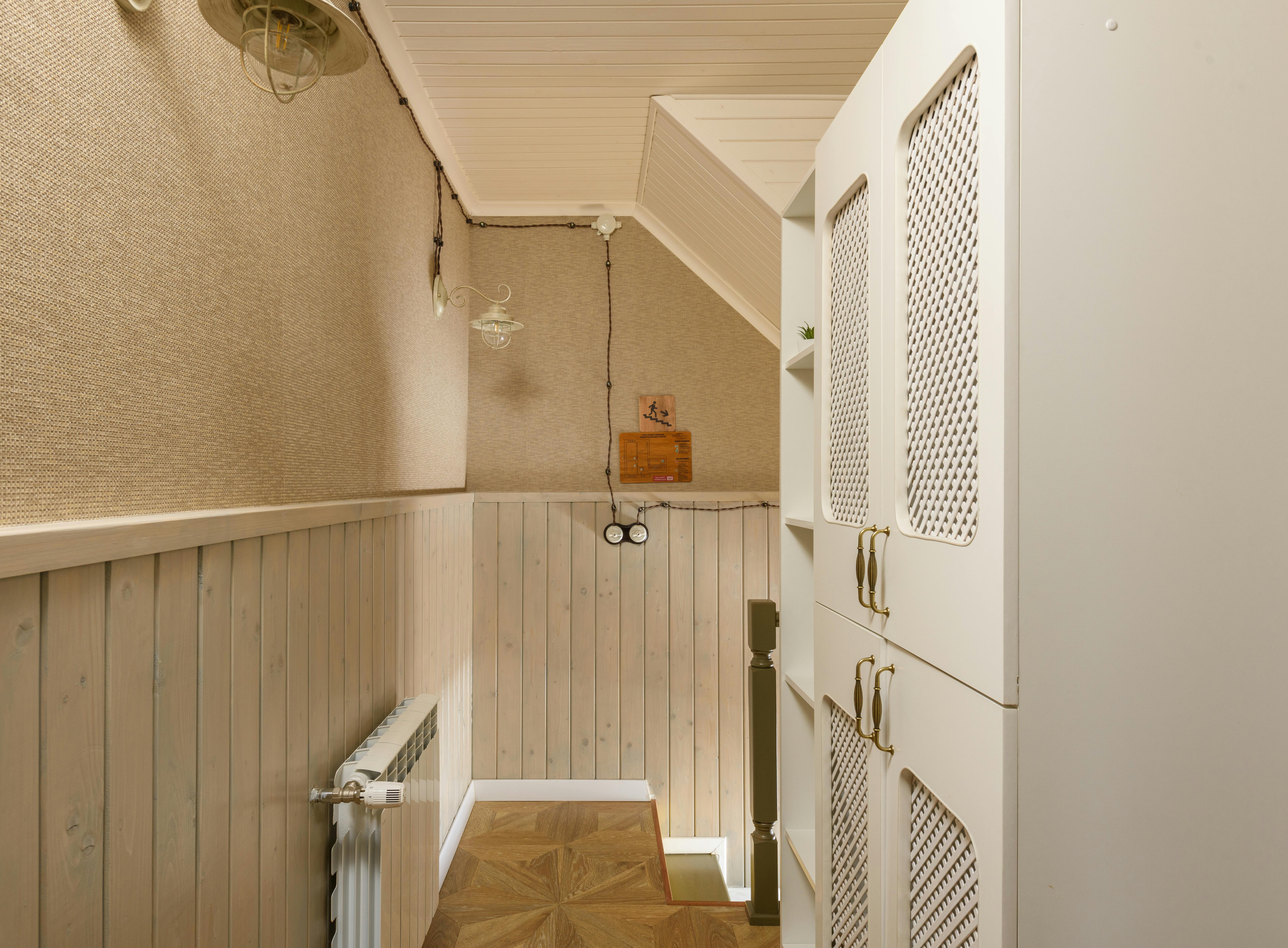 Custom white cabinets with mesh panels and gold handles in a small, well-organized hallway with wood paneling on the walls.